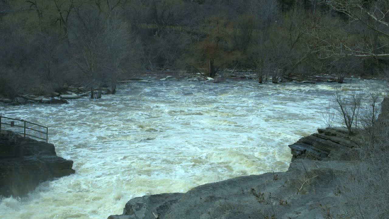 Water along a rocky river fills a basin at the bottom of a set of rapids. Slow motion