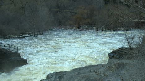 water along a rocky river fills a basin at the bottom of a set of rapids. slow motion