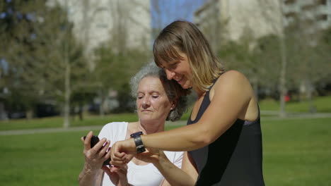 Two-women-comparing-time-on-digital-devices-in-summer-park.