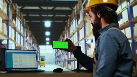 el gerente del almacén mira la pantalla verde en el teléfono inteligente