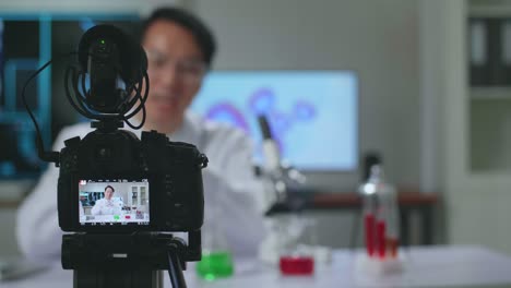 asian scientist researching in the laboratory with a microscope and speaking to the camera