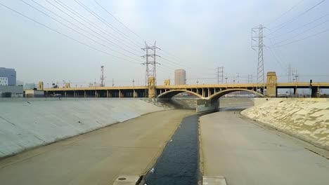 Centro-De-La-Río-Canal-De-Agua-De-Hormigón-De-Control-De-Inundaciones-Urbanas-Históricas-Hacia-El-Puente-Del-Viaducto-Urbano,-Vista-Aérea