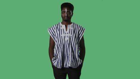 portrait young african american man seriously looking at the camera. black male with an ethnic white pattern on face and in striped national shirt posing on green screen in studio