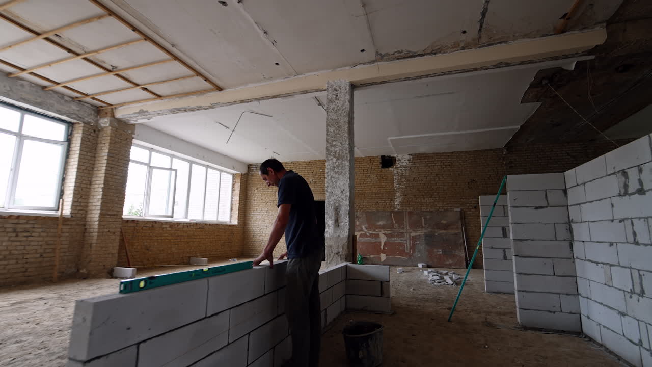 Builder working inside the large spacious room. Man building a wall of white long bricks.