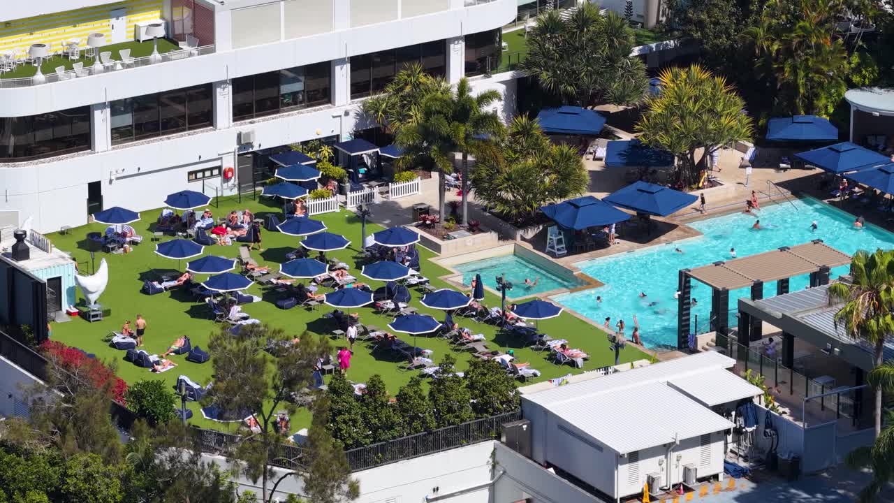 Drone captures sunbathers, umbrellas, and swimming pool at luxury resort under bright daylight