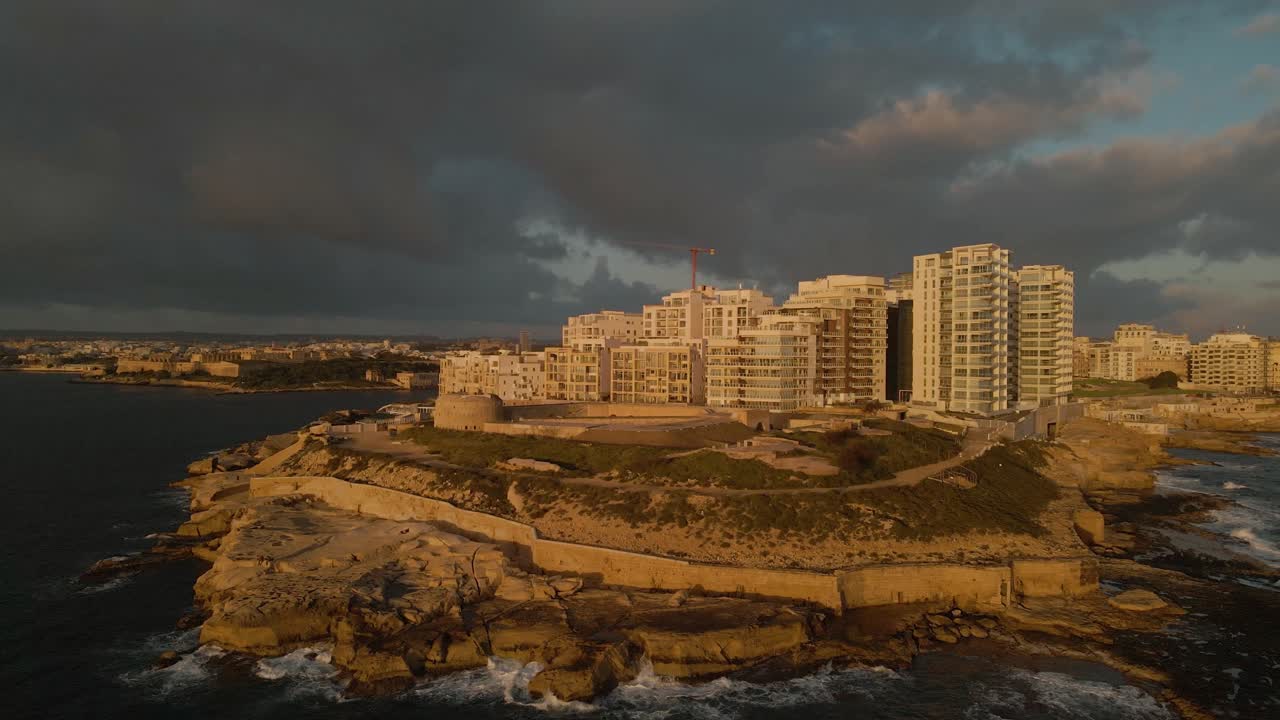 Vista aerea cinematografica su Forte Tigné all'alba, con una calda luce mattutina e nuvole grigie sullo sfondo che creano un'atmosfera drammatica e misteriosa, Sliema, Malta (riprese con drone)