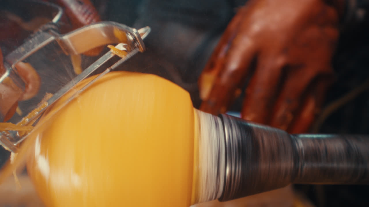 Close-up of hands peeling a ripe persimmon with a metal vegetable peeler, bright orange fruit and juice