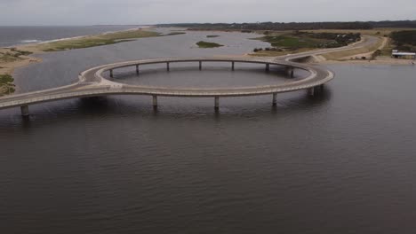 Four-wheel-driving-on-circular-bridge-at-Laguna-Garzon-with-two-kitesurfers-in-background,-Uruguay