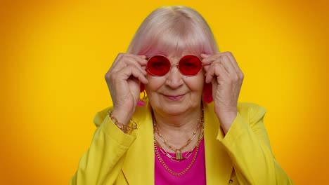 feliz juguetona anciana abuela mujer con gafas de sol rojas parpadeando el ojo, mirando a la cámara con una sonrisa