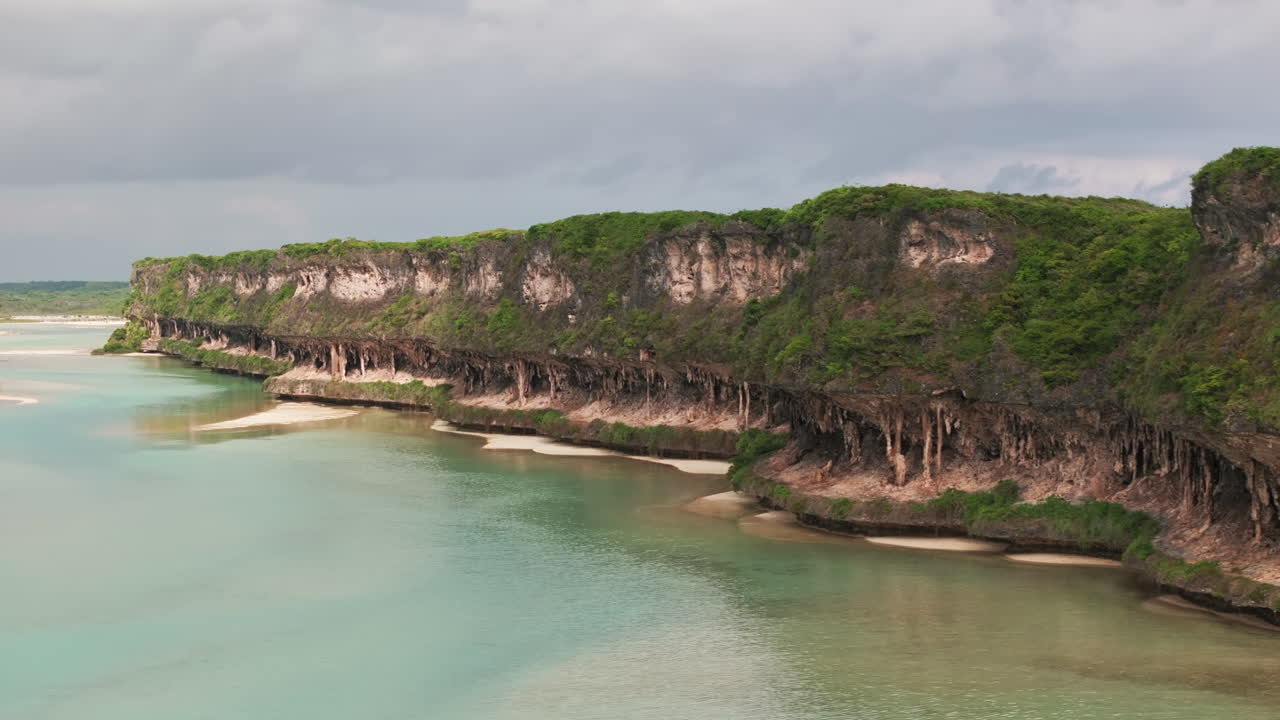 Aerial view of Lekini Bay, Ouvéa, featuring turquoise waters, coral reef formations, limestone cliffs and lush tropical vegetation along the coastline