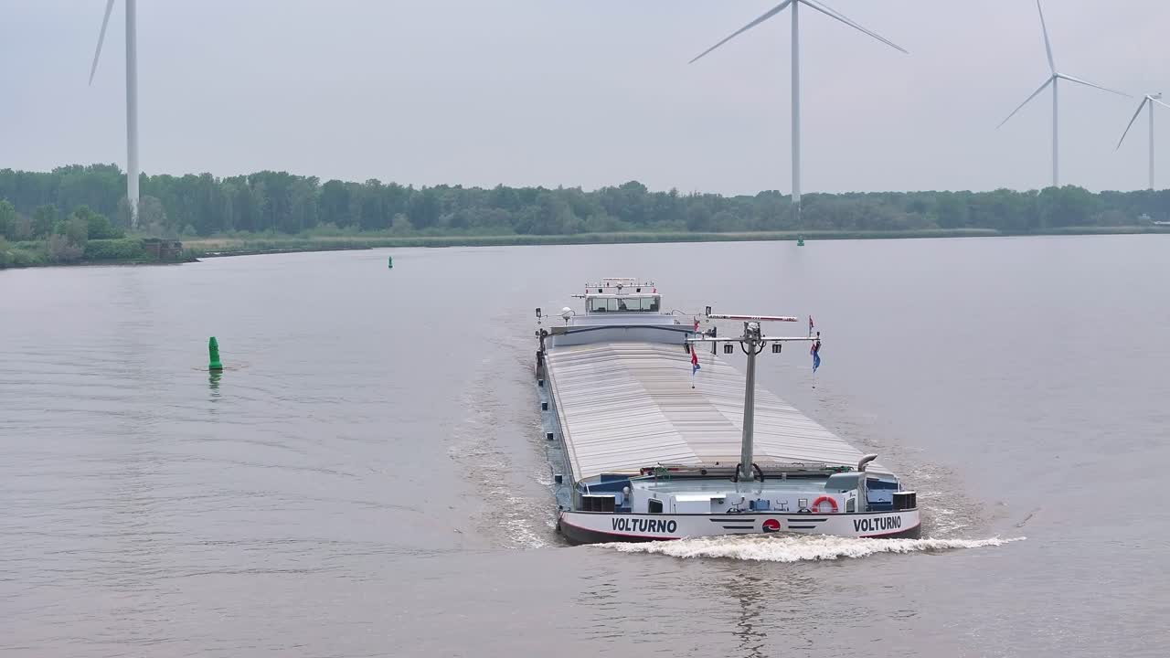 Cargo Ship VOLTURNO Sailing on a River with Wind Turbines