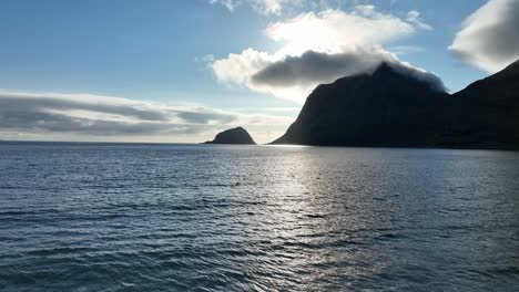 drone glides forward just above sea at haukland beach in lofoten, moving toward sunset, calm waves and misty silhouetted mountains