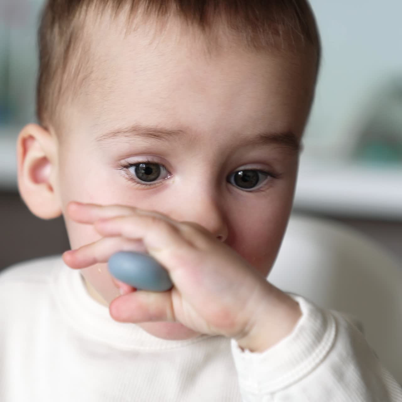 Lovely Caucasian baby boy with pieces of food on his face. Little child eating from spoon himself. Close up