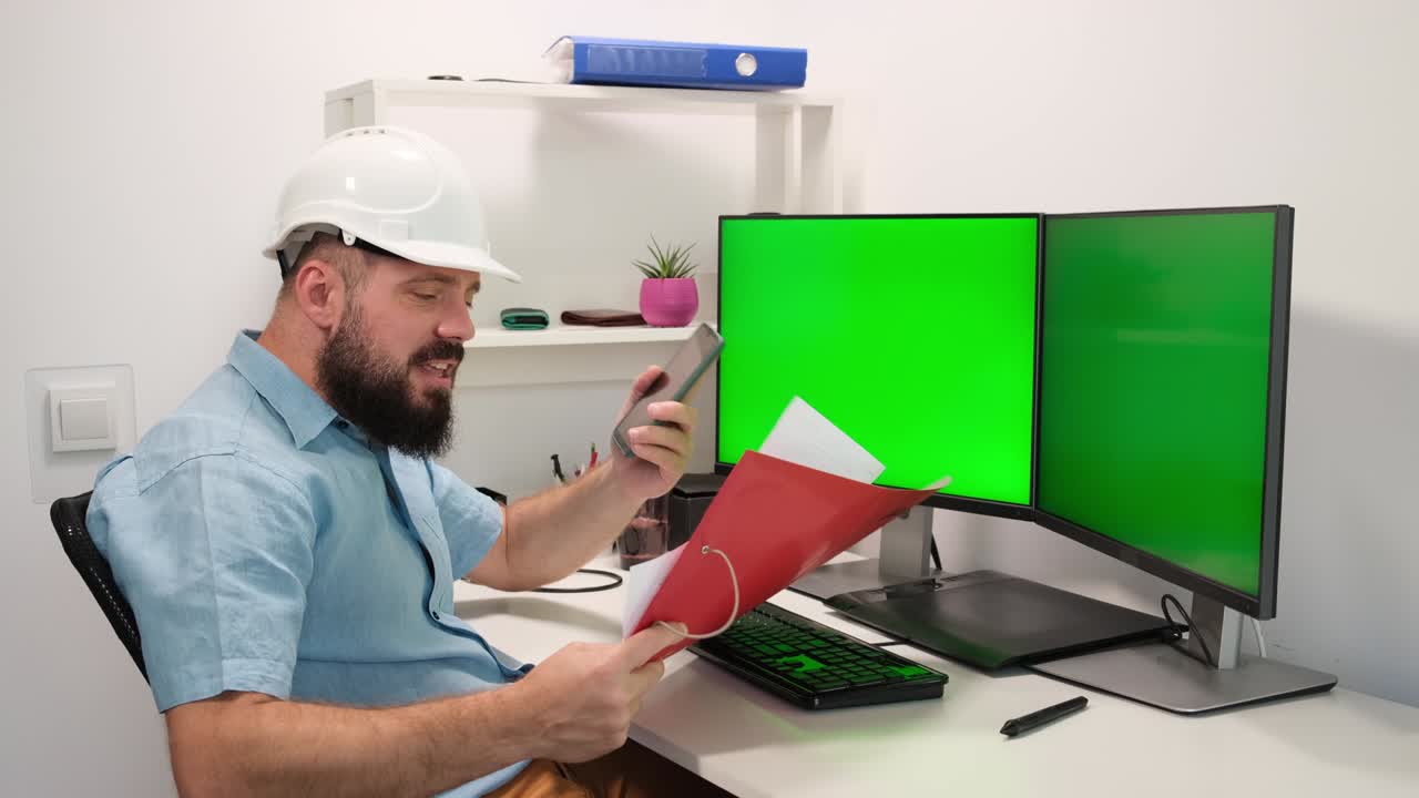 hombre con casco trabajando en casa detrás de una computadora con dos pantallas verdes para rastrear y pegar su información. interior acogedor de la casa, alto concepto tecnológico.