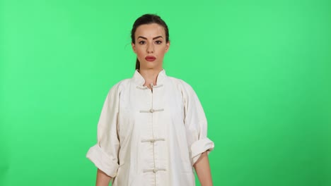 Young-caucasian-woman-in-white-kungfu-wushu-uniform-practicing-martial-arts-and-salutation-while-looking-in-camera