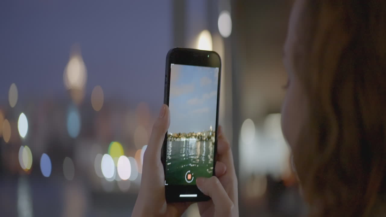 persona tomando una foto del horizonte de la ciudad por la noche junto al río