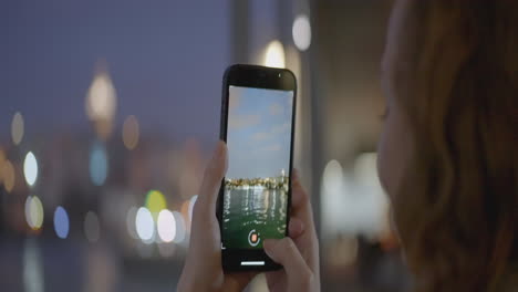 persona tomando una foto del horizonte de la ciudad por la noche junto al río