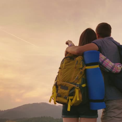 a young couple of tourists with backpacks look up at the airplane in the sky