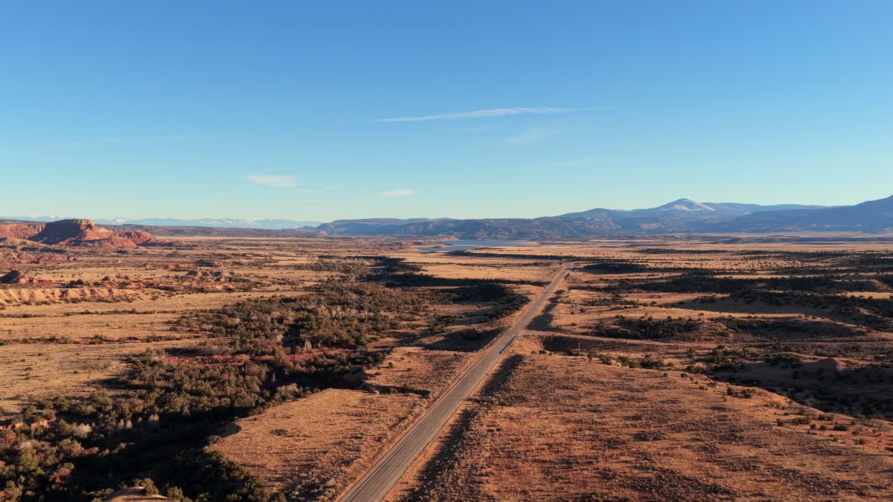 High-end drone-opname van een lange snelweg die een uitgestrekt woestijnlandschap in het zuidwesten doorkruist tijdens het gouden uur. Perfect voor reisdocumentaires en autoreclames die een grote schaal nodig hebben