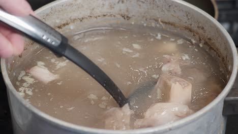 messy unappetizing bone brooth in aluminum pan, scooping up and stiring in slow motion