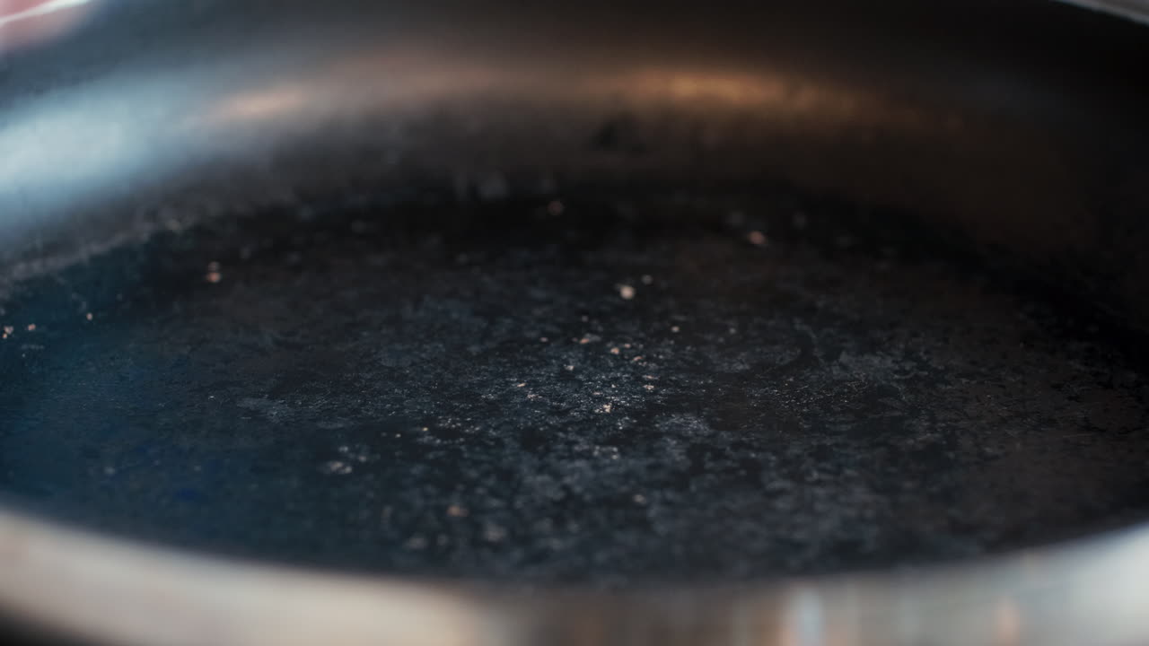 Close-up of chef hand spraying non-stick cooking oil onto a hot stainless steel skillet for food preparation