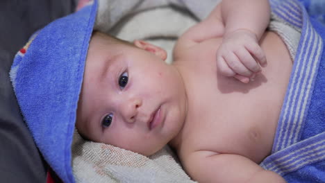 healthy caucasian child lying peacefully covered in towel. beautiful little kid looks aside waving tiny fist. close up.