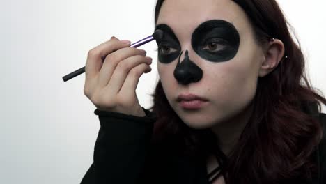 una mujer joven usa un pincel para aplicar sombras para el maquillaje de santa muerte.