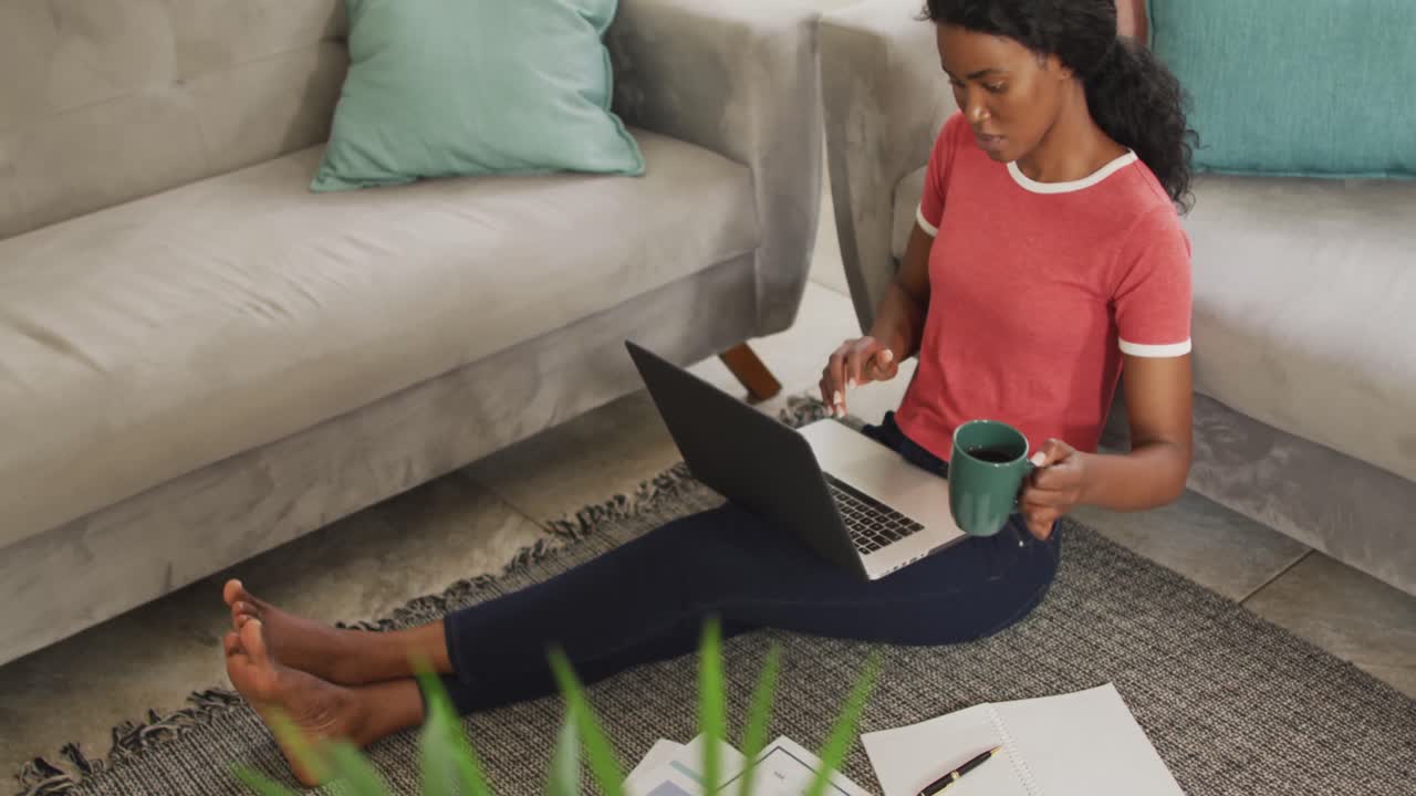 Video of happy african american woman sitting on floor using laptop
