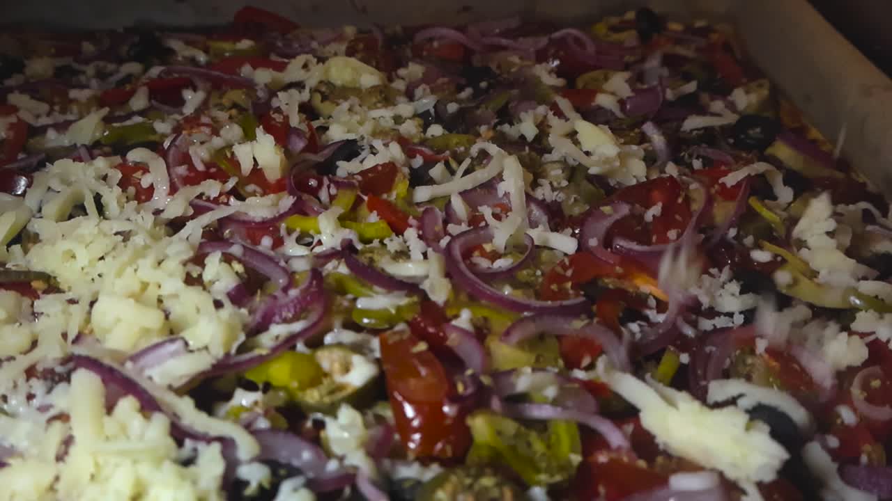 Close up view of golden yellow cheese falling on a freshly made pizza that is steaming hot. Cheese falls and drops on other droppings like onions, jalapenos, paprika and meat on the home made pizza