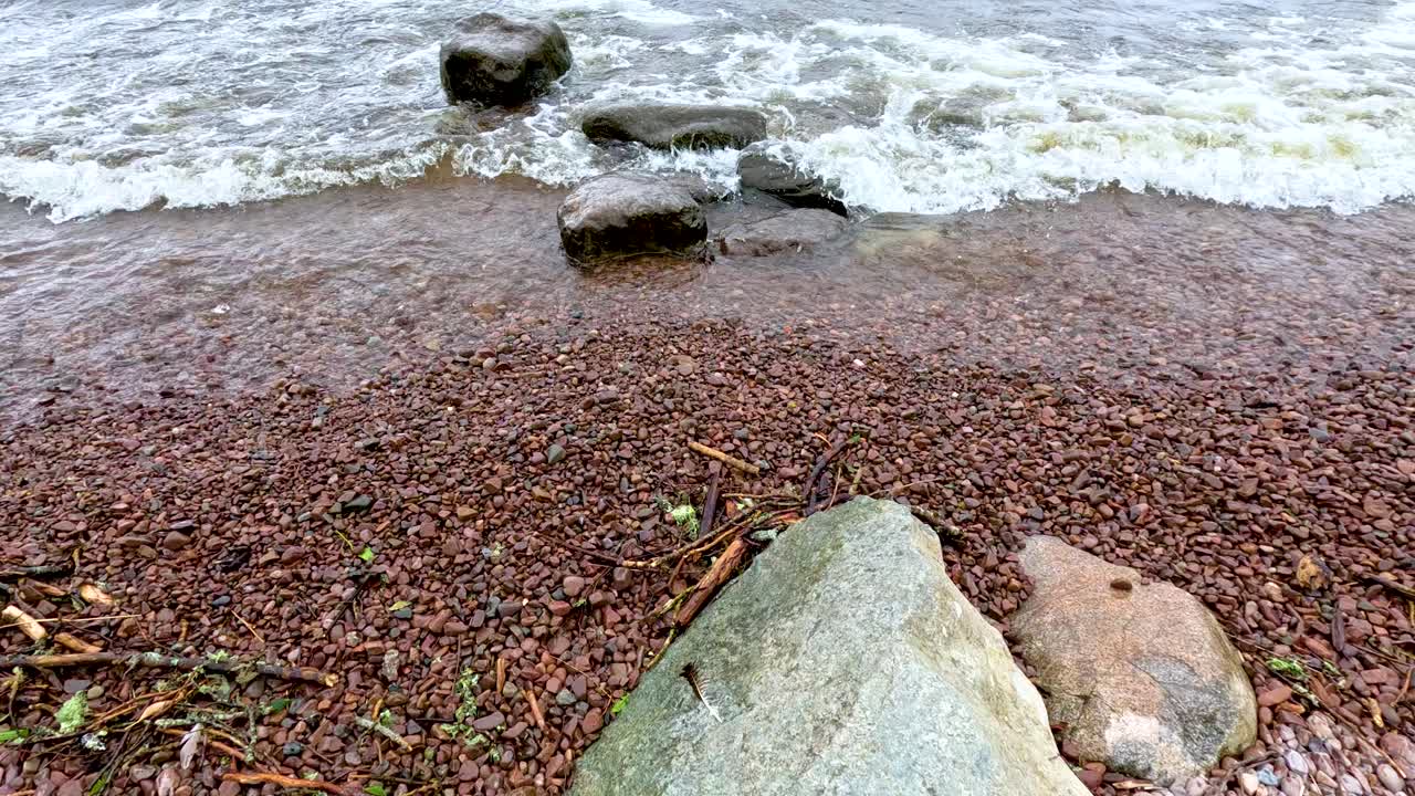 Overhead view of gentle waves washing over a rocky, pebbled shoreline at Loch Ness, Scotland