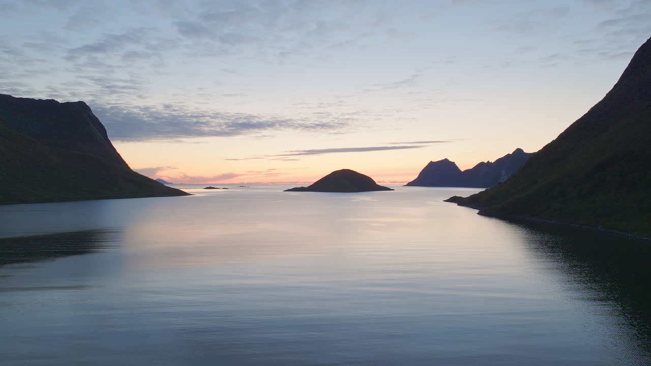 Smuk gul og blå solnedgang over idyllisk havvand og silhuetter af bjerge, luftfoto.