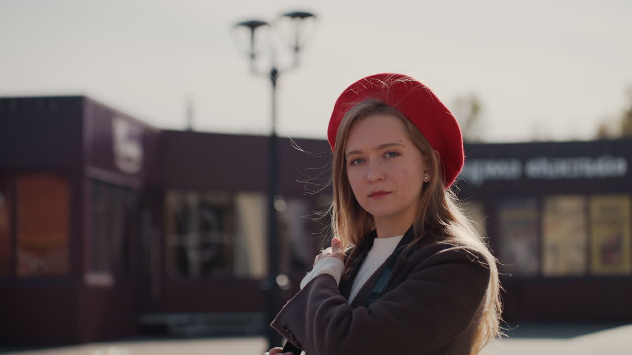Donna in abiti caldi osserva le foglie autunnali. Donna con giacca di lana guarda il vivace fogliame colorato d'autunno. Donna alla moda con cappello rosso ammira le foglie arancioni brillanti in un mercato all'aperto.