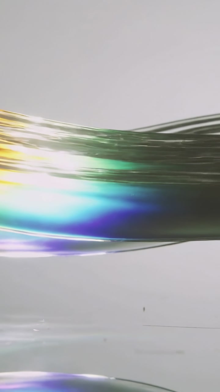 Vertical video: Sliding rainbow film rippling on tabletop, catching offframe light, reflecting