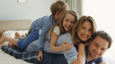 vista de cerca de padres e hijos alegres acostados uno en la parte posterior del otro en la cama y sonriendo a la cámara