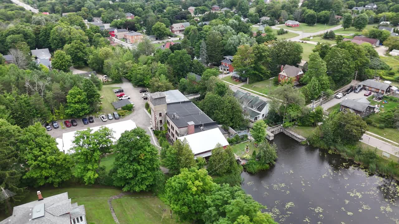 Aerial view of the historic Alton Mill in Alton, Ontario, surrounded by lush trees, heritage homes, and the millpond, showcasing the village’s cultural and architectural charm