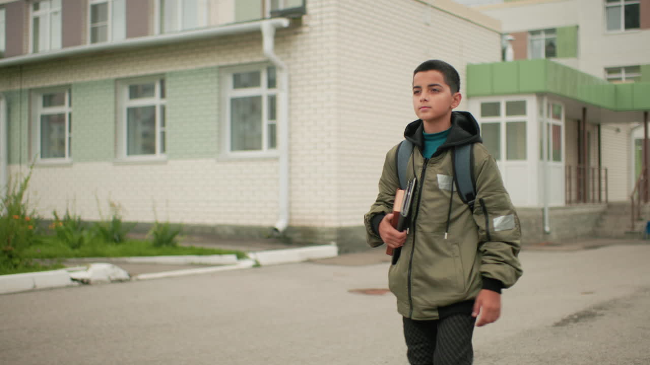 한 남자아이가 매일 학교에서 책과 태블릿을 팔에 끼고 어깨에는 백팩을 멘 채 집으로 향하며 학업에 대한 결의와 책임감을 보이는 모습이에요.