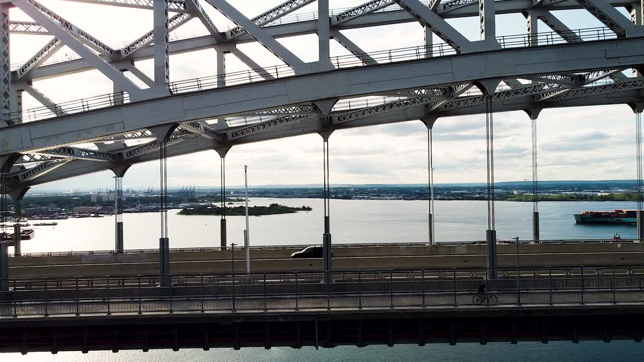 People and cars crossing the Bayonne bridge with cargo ship in the distance near New York City - right to left pan aerial footage
