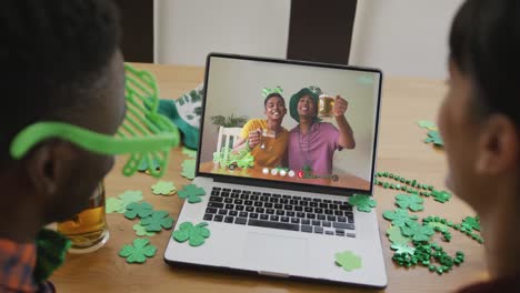 amigos afroamericanos sonrientes con cerveza vistiendo objetos en forma de trébol en una videollamada en una computadora portátil