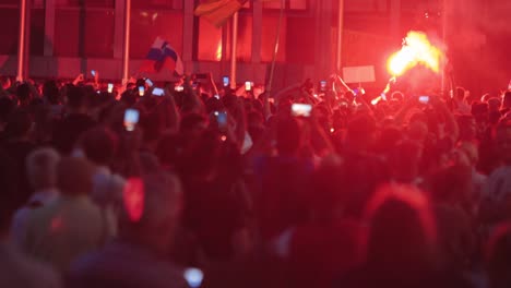 protesters with flags, smartphones, and firework at night. anti-corona measures protest in ljubljana, slovenia. medium shot