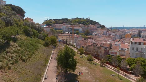 Vista-Aérea-Del-Jardín-Verde-De-Cerca-Da-Graca-Con-El-Castillo-De-San-Jorge-Al-Fondo,-Lisboa