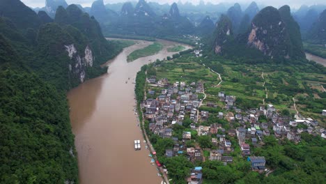 Toma-Aérea-Inclinada-De-La-Antigua-Ciudad-De-Xingping-Junto-Al-Río-Li-Con-Un-Paisaje-Montañoso-Kárstico-En-El-Fondo,-China