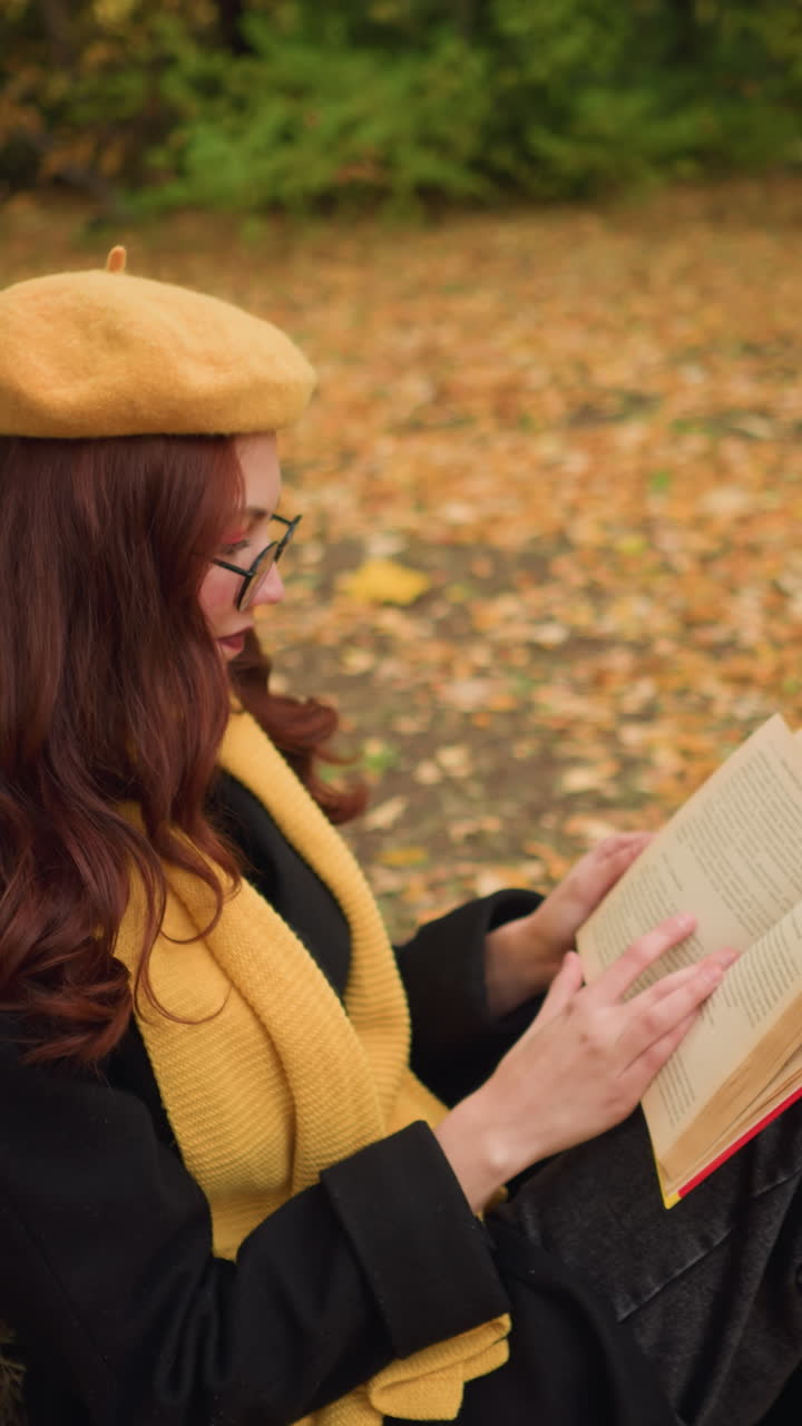 estudiante con boina amarilla y bufanda se sienta al aire libre apoyándose en un árbol, repasando pensativamente las páginas de los libros, rodeada de hojas doradas de otoño, parece involucrada en una lectura pacífica y reflexiva