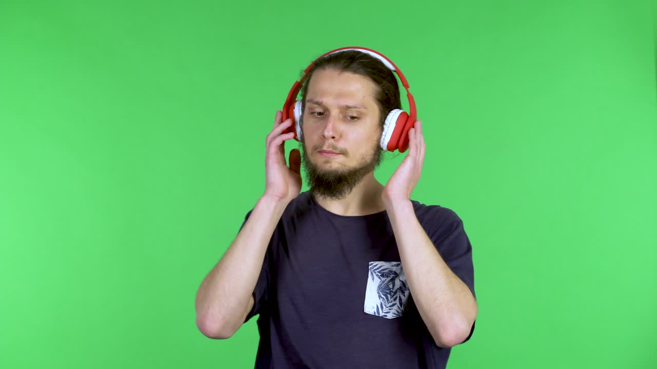 un joven de pelo oscuro barbudo disfruta escuchando música con grandes auriculares rojos, canta junto a la música y baila. un hombre en una pantalla verde en el estudio. cerca