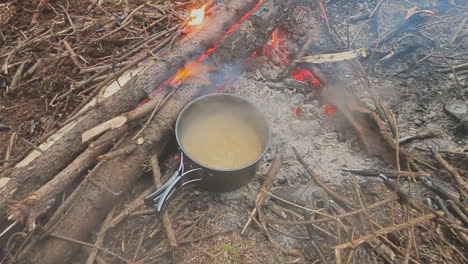 Lid-lifted-from-pasta-noodles-boiling-in-pot-over-campfire-coals