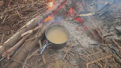 lid lifted from pasta noodles boiling in pot over campfire coals