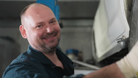 engineer in blue uniform with white gloves smiling as he aligns car tire for optimal performance in auto repair workshop, using tools for precision