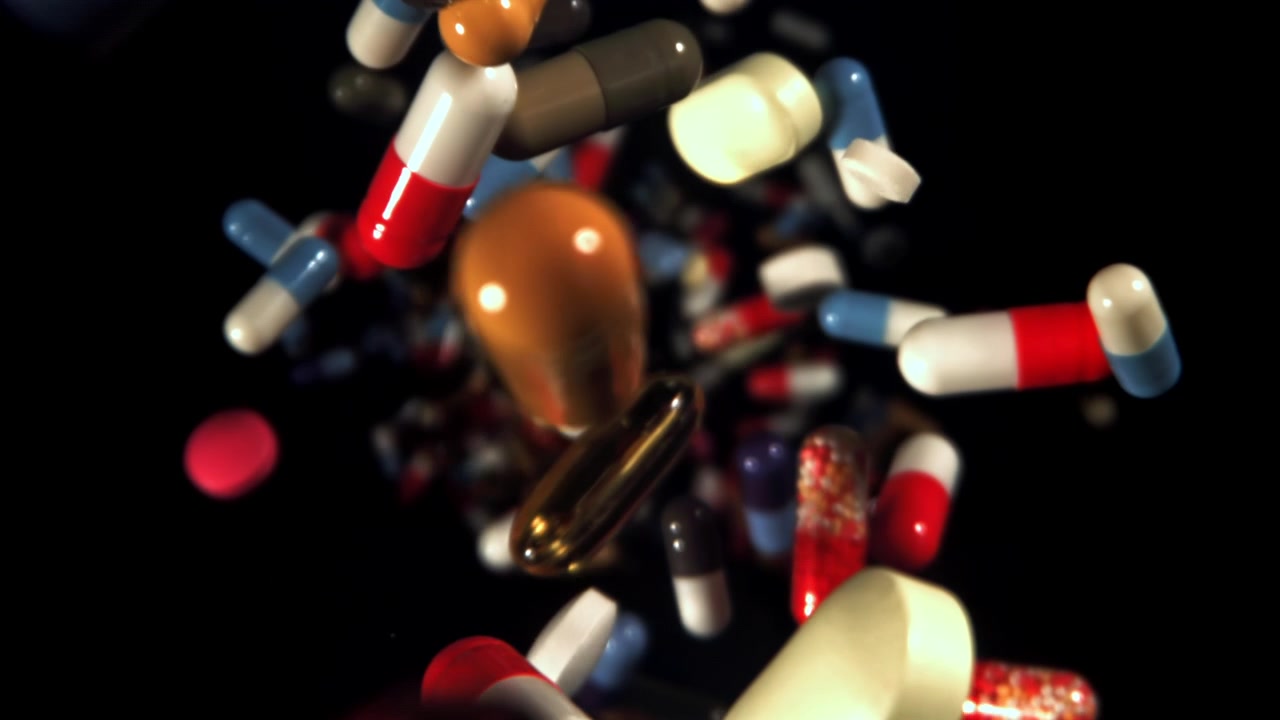 Pillole e capsule colorate che cadono al rallentatore su sfondo nero