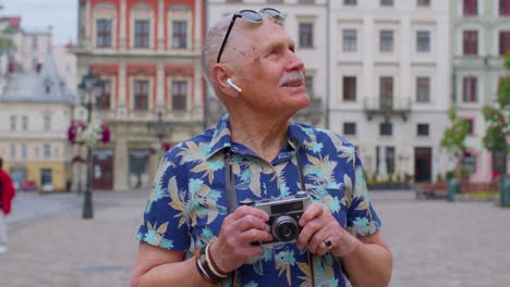 senior man tourist with retro photo camera, smiling, listening music earphones, dancing on street