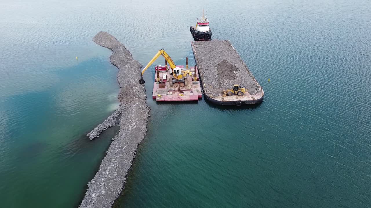 excavadora en barcaza en agua construyendo rompeolas de rocas cerca de la costa