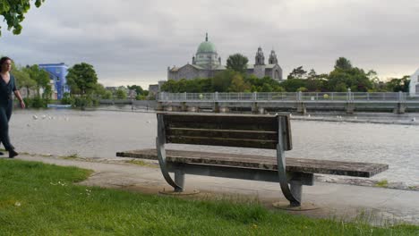 galway girl walks along riverwalk pass wooden bench on windy day, ireland